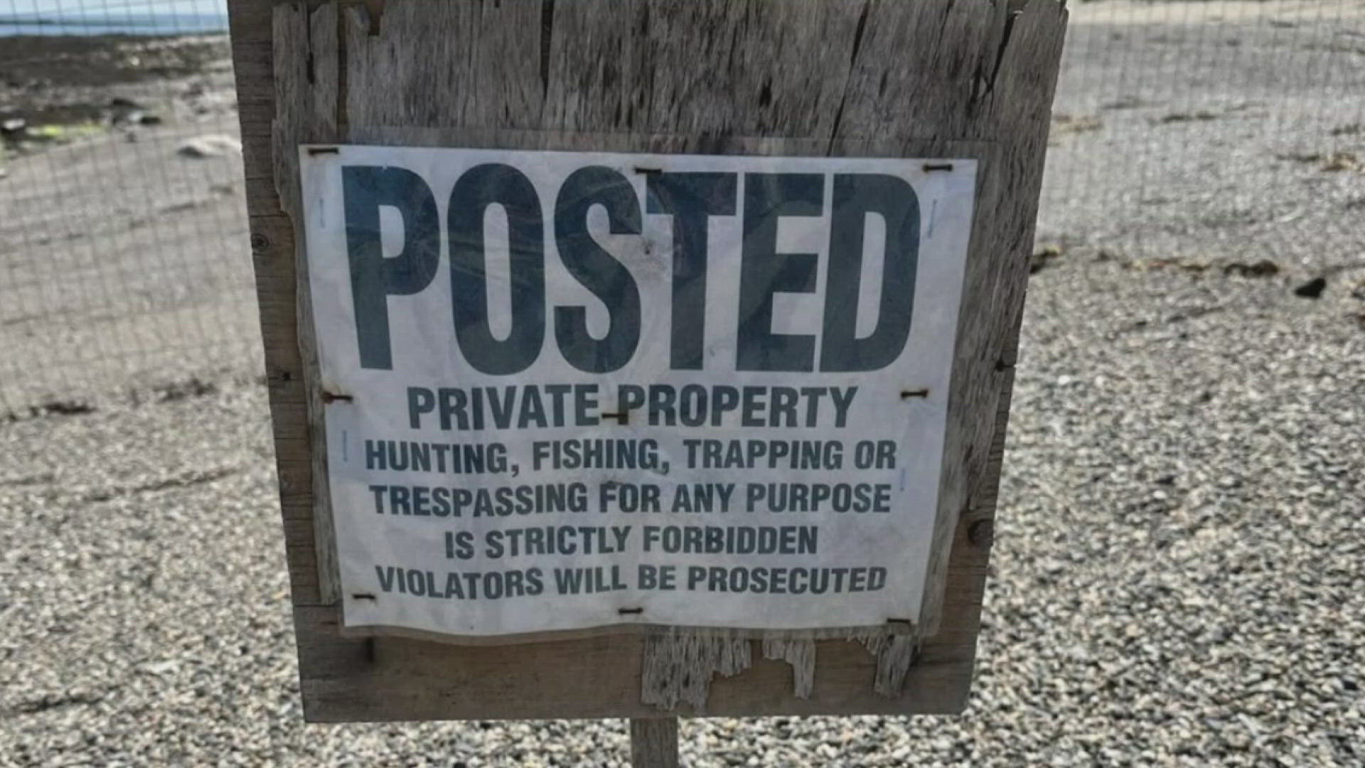 A sign prohibiting fishing, hunting, trapping, and trespassing was planted in the rocky sand along Crescent Beach, but some question whether the sign is legal.